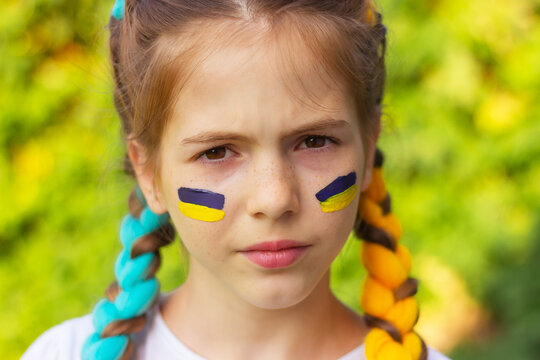 the face of a girl with yellow-blue national Ukrainian flags painted on her cheeks. concept of Ukrainian patriotism, independence day. sports and fan support.