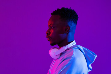 Side view portrait of young handsome African millenial man with headphones in purple futuristic neon light studio background