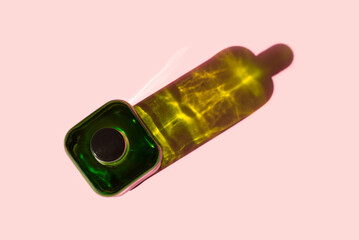 Top view of a green glass bottle on a pink background. Harsh shadow from an object illuminated by sunlight.