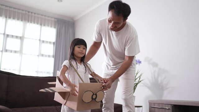 asian little girl playing with cardboard toy airplane with father at home