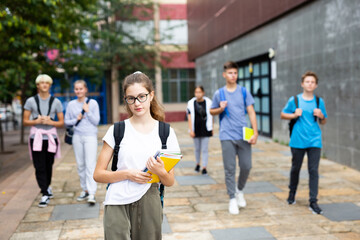 Portrait of female teenage student with workbooks in hands on her way to college on autumn day. Back to school concept.