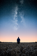 Man standing on wheat field under the stars of the milky way at night. Man looking at stars and dreaming.