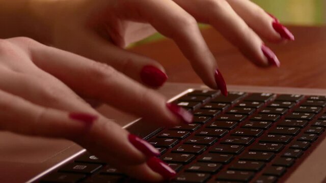 Woman with bringht red nails typing on a dusty laptop keyboard with a Russian-language layout. Hands close-up...Unmodified camera color.