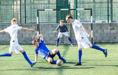 Fototapeta premium Game moments of football match between two teams of teenagers in white and blue shirts