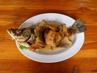 deep-fried snapper fish topped with fish sauce on white dish on wooden table, delicious Thai food...