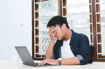 Young Asian man feeling stress and confuse when work laptop on table.