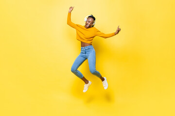 Jumping portrait of happy energetic young African American woman wearing headphones listening to...