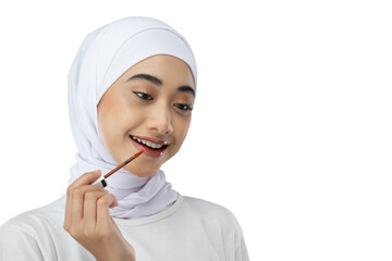 smiling asian veiled girl wearing white dress using lipstick to apply makeup on gray background