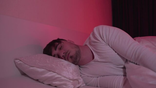 Young Tired Man Sleeping in Bed in His Bedroom. The Room Is Lit Red From A Night Lamp. Cozy Sleep at Your Home. Sleep and Rest concept