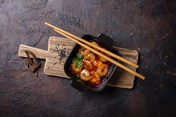 Tasty bright seafood. Cast-iron grill pan of fried shrimps in spicy asian red sauce with chopsticks