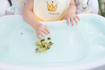 Focus on hand of baby wearing baby apron sitting on dining table eat broccoli by her self, Baby-Led...
