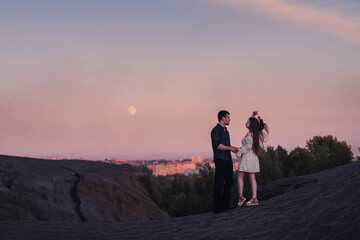 Loving couple embracing and looking moon and city oin sunset