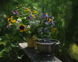     A bouquet of flowers and berries in a dish stand on a wooden board. 