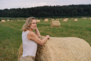 Naklejka na ściany i meble young beautiful caucasian lady with blond hair lean on haystack looking aside standing in summer field