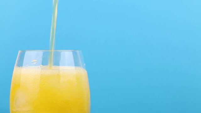 Filling a glass with yellow soda on a blue background