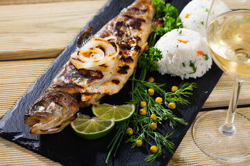 Delicious baked trout fish served with white wine on black board with garnish of white rice,...