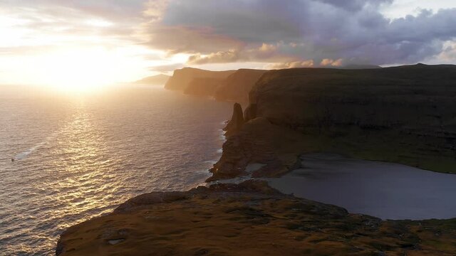 Aerial view of beautiful orange sunset in Faroe Island. Huge cliff and sea stacks glow in golden evening light