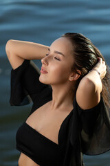 Naklejka na ściany i meble Portrait of a beautiful woman with wet hair in a sexy black bikini against the backdrop of the sea and sunset. fashionable stylish young woman on tropical beach