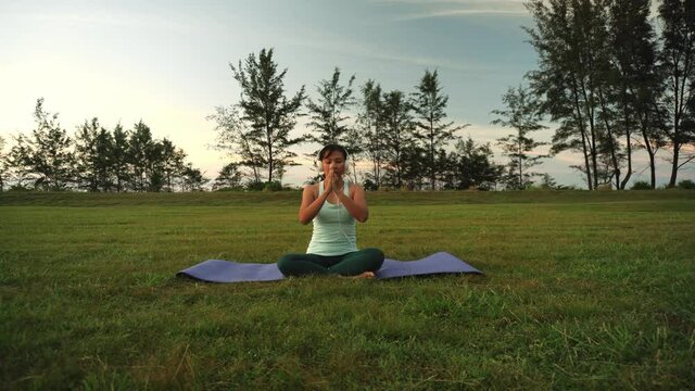 Woman sitting outdoor and doing yoga with headset on - concept of fitness people and music