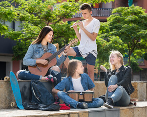 Company of happy teenagers musicians with instruments in park on summer day