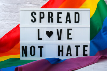 Rainbow flag with lightbox and text SPREAD LOVE NOT HATE. Rainbow lgbtq flag made from silk material. Symbol of LGBTQ pride month. Equal rights. Peace and freedom