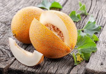 Ripe yellow melon with slices and melon leaves on a old wooden table.