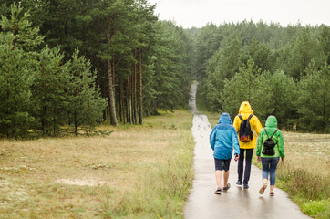 Fototapeta premium Three people walk on the footpath during the rain.