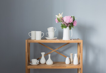 white cups and flowers on vase  on wooden shelf on gray background