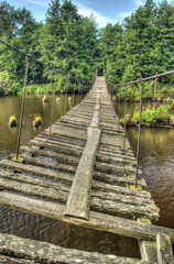 Old and damaged rope and wooden boards bridge over the river Irbe, Latvia.