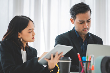Businesswoman discussing charts and graphs showing on tablet screen with friend with smiling faces in the meeting room. Brainstorming and teamwork concept.