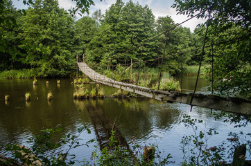 Fototapeta premium Old and damaged rope and wooden boards bridge over the river Irbe, Latvia.