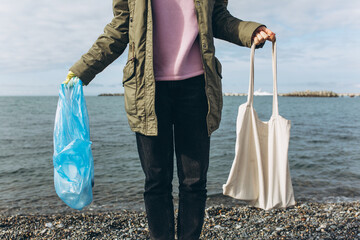 A female volunteer holds a garbage bag and a reusable canvas bag in her hands. The concept of waste recycling, taking care of the environment.