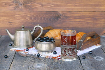 A glass mug of black tea near a tray of croissants and bowl of fresh berries on a wooden background.  