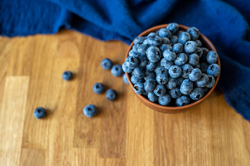 Blueberries in clay bowl  next to blue towel on a wooden background, top view