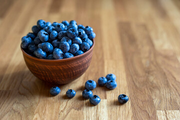 Blueberries in clay bowl on a wooden background, close up