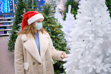 A woman in a medical face mask chooses a faux Christmas tree in a store with New Year gifts