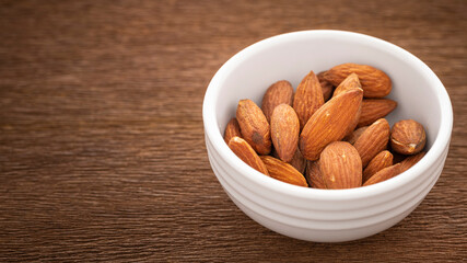 roasted salted almonds in simply white ceramic bowl on rustic natural wood texture background, full HD ratio