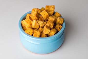 Square-shaped bread crumbs in a blue pot on a white background. Oven-fried golden brown bread crumbs.