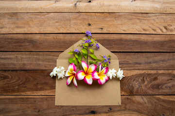 flowers frangipani, jasmine, purple and bamboo leaf arrangement in brown envelope flat lay postcard style on background wooden