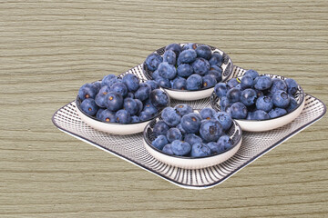Closeup of a decorative plate with four bowls with fresh blueberries on a rustic wooden table. Concept of healthy nutrition. Space for your design.