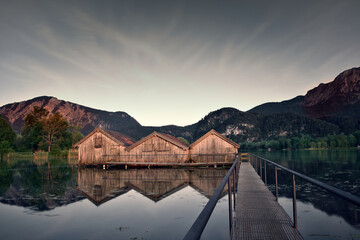 Kochelsee in den Alpen in Deutschland: Bootshäuser mit Reflektion, ruhige Stimmung bei Sonnenuntergang
