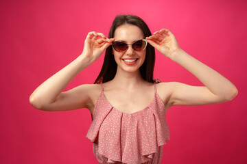 Young casual brunette woman in sunglasses against pink background