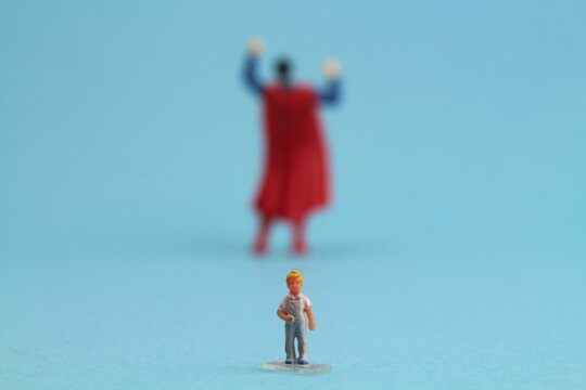 Figur von einem kleinen Jungen steht vor einer Superhelden Figur 