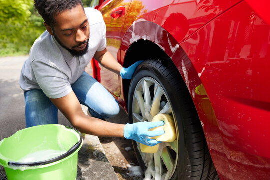 Man Washing Wheels Of Car During Valet Using Bucket And Sponge
