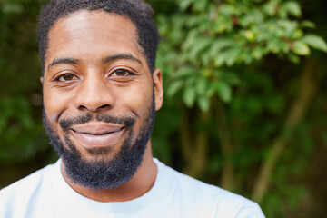 Obraz premium Head And Shoulders Portrait Of Smiling Young Man Standing Outdoors In Garden