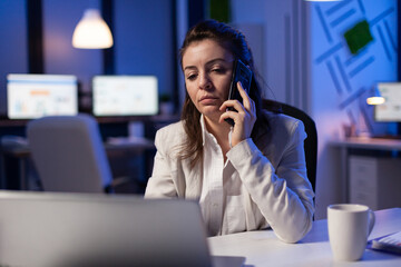 Tired corporate freelancer having conversation on phone while working exhausted for economic statistics in business office late at night Focused employee using modern technology network wireless