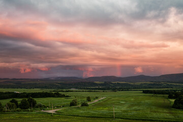 Fototapeta na wymiar pink and lilac storm clouds at sunset and a green meadow