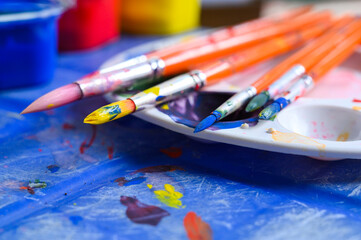 Painters brushes on plastic palette with colorful watercolour on brown paper. Copy space
