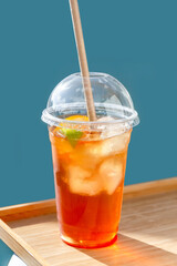 Cold fruit tea with a ice in a plastic cup with a lid on a wooden tray. Take away. Poster. Photo. 