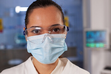 Portrait of biotechnology chemist working in laboratory at medical hospital. Woman with scientist occupation wearing protection glasses, face mask and lab coat industry equipment